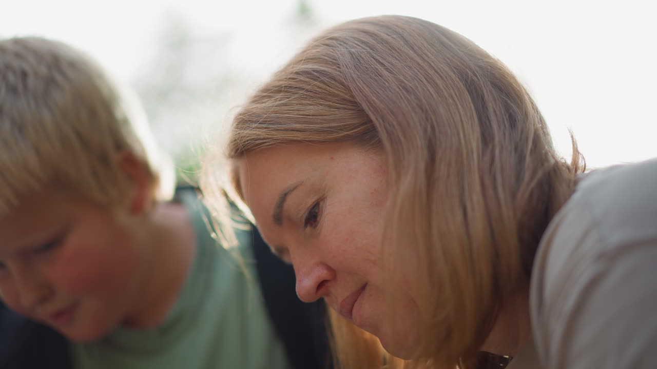 White Mother Leaning Over Homework Table, Focused Expression As She Helps Blonde Son With Reading And Problem Solving In Cozy Indoor Kitchen Setting Candid Portraits Capture Tender Guidance, Concern