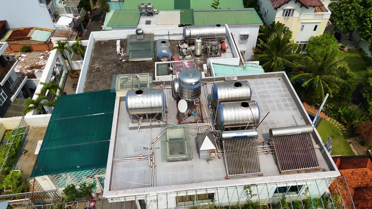 Drone orbit shot of a residential rooftop in Ho Chi Minh City, Vietnam, featuring water tanks, solar panels, and urban greenery in a densely packed neighborhood.