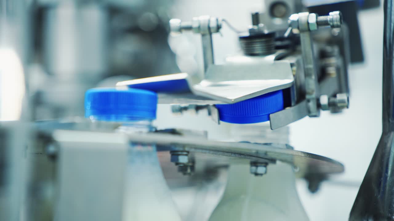 Automated machine covering plastic bottle with lid. Dairy production. Mechanical process of putting cover on a bottle with milk in a modern factory.