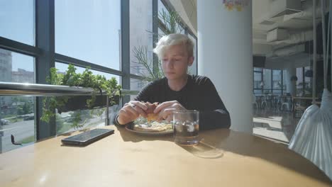 man eating burger and drinking at cafe with city view