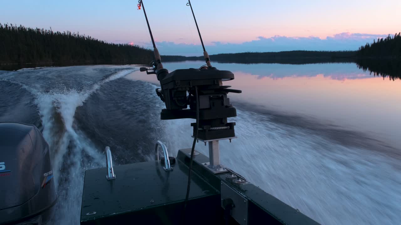 Side view of a fishing boat speeding on a calm lake with a colourful sunset view