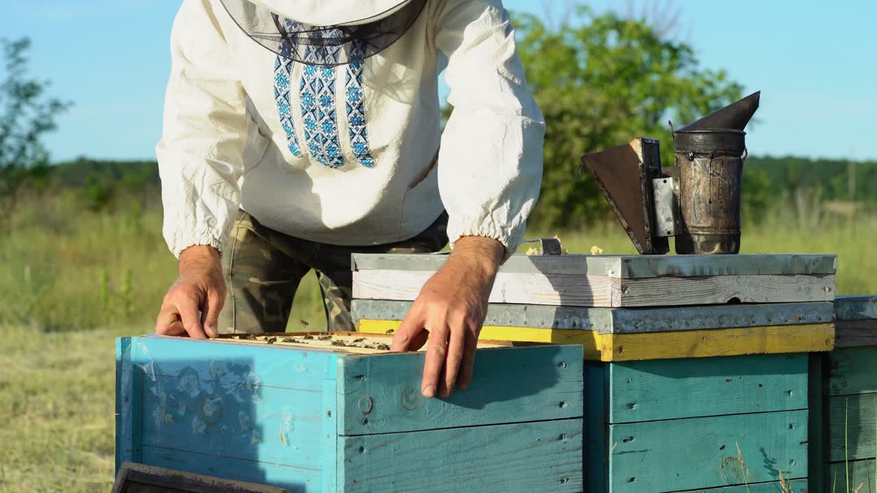 Man beekeeper puts one new frame into the hive full of bees and closes with hood on the natural background. Apiarist working outdoors on his bee-garden in summer. Apiary concept