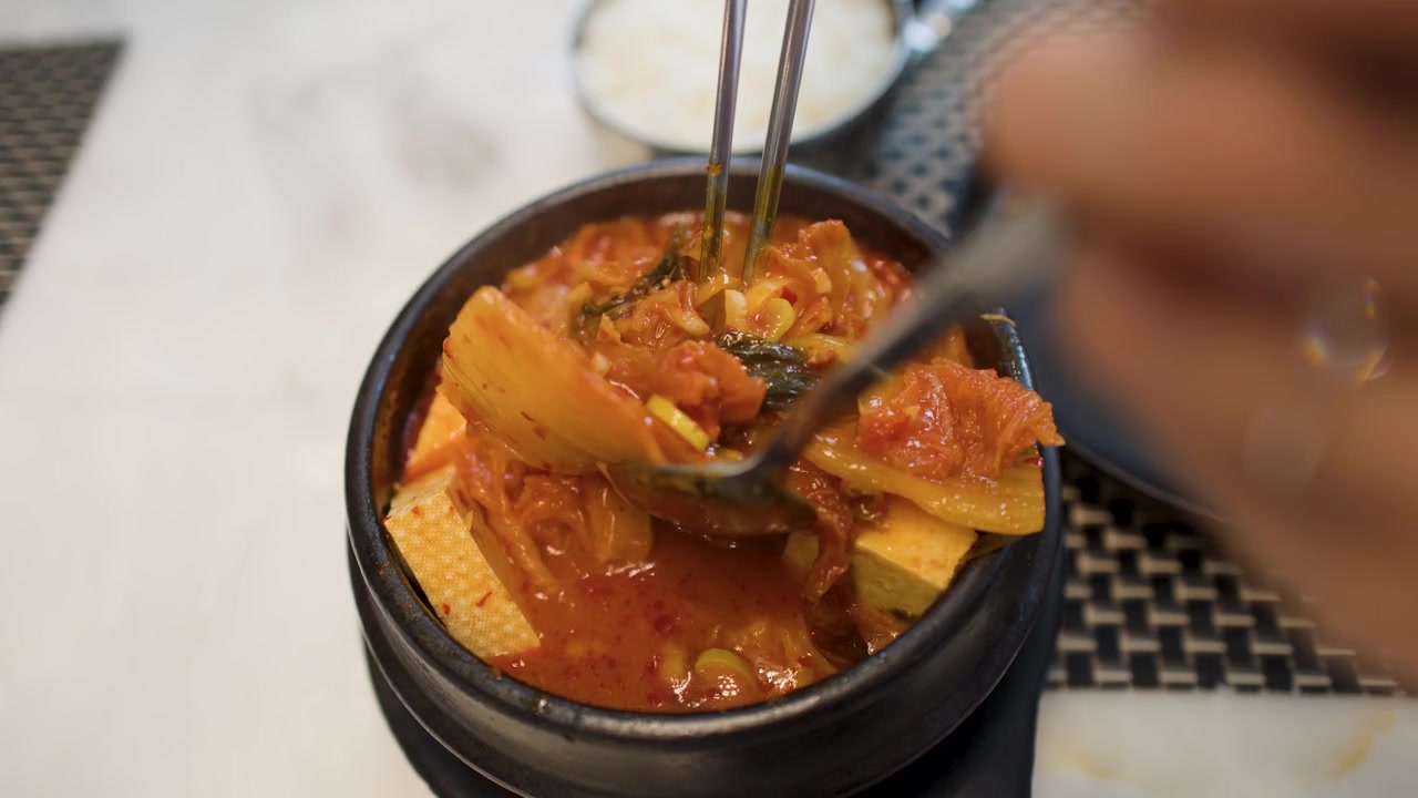 Bidikan close-up tangan yang menggunakan sendok untuk makan sup tahu kimchi Korea panas