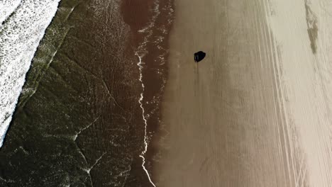 aerial view of a lonely black car driving on sandy beach during golden hours, off road vehicle between ocean waves and sand dunes