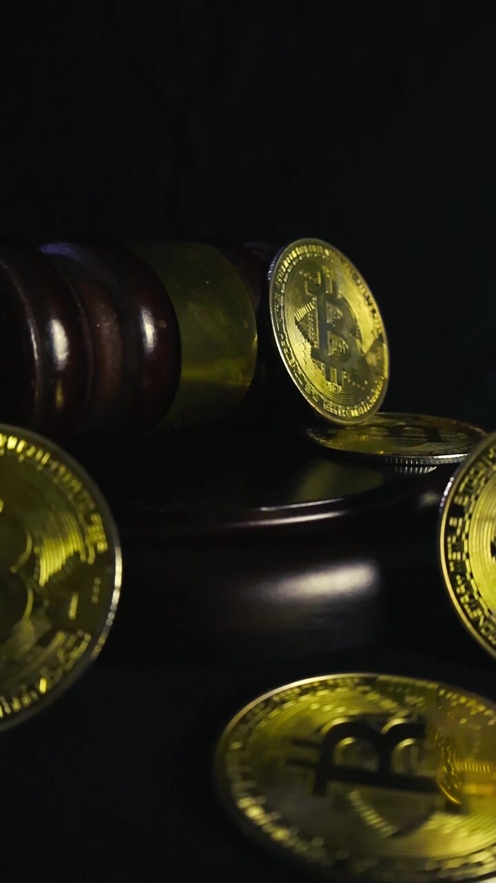 Bitcoin fisici dorati attorno a un martelletto da giudice in legno su uno sfondo nero scuro, che simboleggiano la regolamentazione delle criptovalute, le questioni legali e i concetti di criminalità finanziaria.