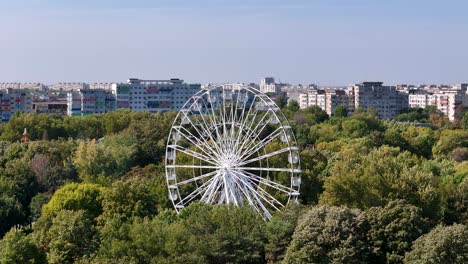 rotating drone view of a ferris wheel in oraselul copiilor park with bucharest's cityscape in the background, romania