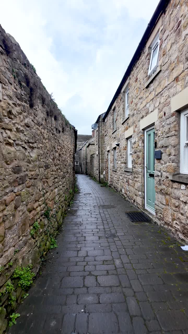 Old stone buildings lining a narrow cobbled street in Barnard Castle, England. vertical video, push forward shot
