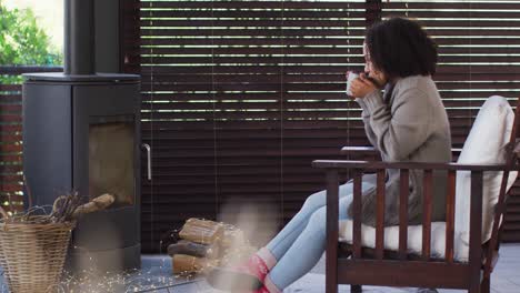 african american woman drinking coffee while sitting near the fireplace at vacation home