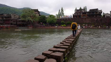 traveler walking across stepping stones in phoenix ancient town, china