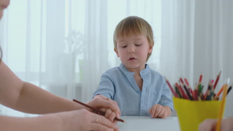 un niño con una camiseta azul sentado en la cocina en la mesa dibuja un marcador
