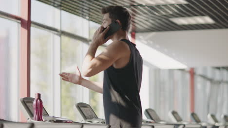 handsome man using mobile phone in gym. strong sportsman jogging on treadmill