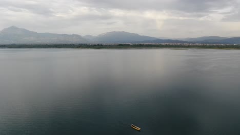 Vista-De-Drones-En-Albania-Volando-Sobre-El-Lago-Shkodër-En-Pogradec-En-Un-Día-Nublado-Con-Montañas-En-El-Horizonte-Y-Un-Barco-Amarillo-En-El-Medio