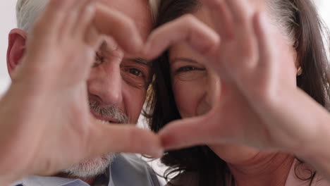 close up happy old couple making heart shape with hands gesturing romantic commitment enjoying loving relationship