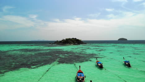 Vuelo-Sobre-Barcos-Anclados-Y-Agua-Clara-Con-Pequeña-Isla-De-Rocas-Al-Final