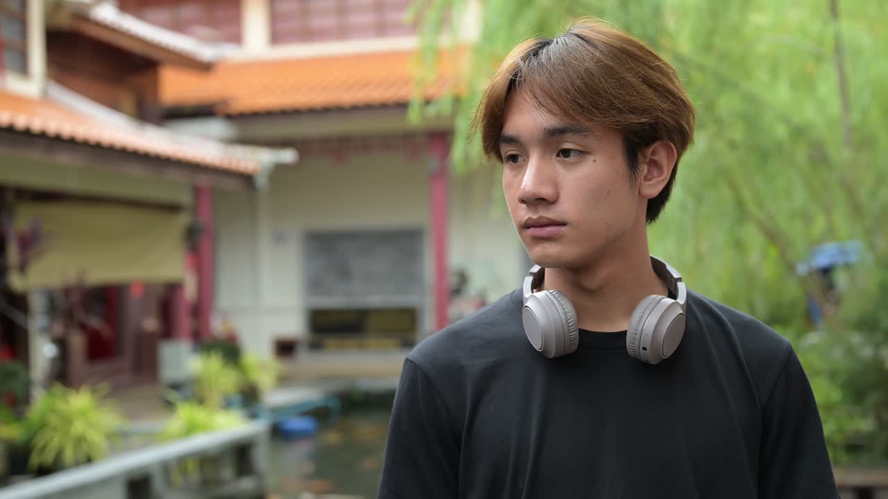 Young Thai Asian man in traditional Asian Zen garden during summer thinking and smiling. Confident, relaxed, and authentic look suitable for various concepts and uses