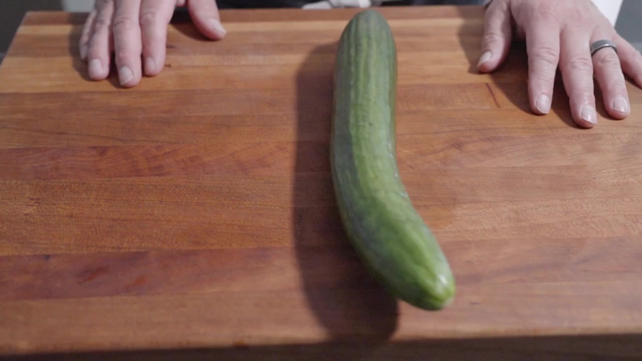 A static shot of a cucumber being rolled onto a cutting board, followed by the chef’s hands placed on the board. Ideal for culinary content, capturing the start of fresh ingredient preparation.
