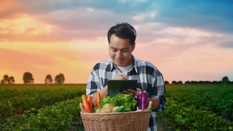 granjero masculino asiático con canasta de verduras tableta de escritura en el campo
