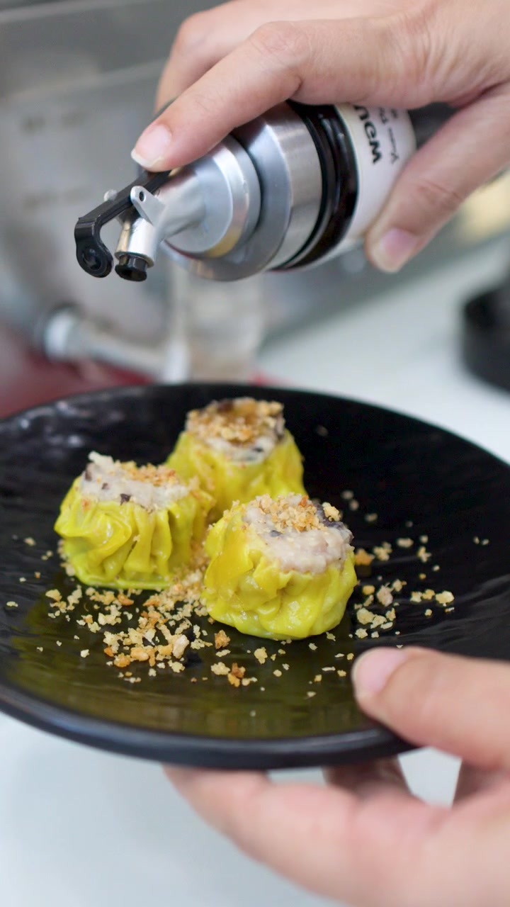 Primo piano di mani che versano salsa scura su ravioli dim sum gialli in un ristorante.