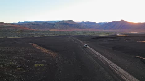 White-SUV-Driving-On-Black-Sand-Terrain-In-Iceland-Countryside-Landscape