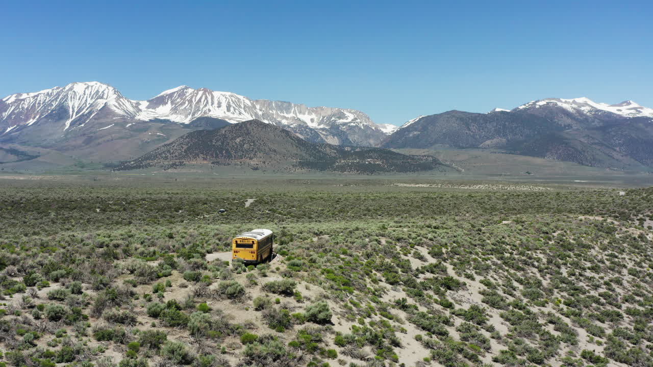 el autobús escolar amarillo viaja a través del desierto remoto con las nevadas montañas de la sierra nevada en el fondo