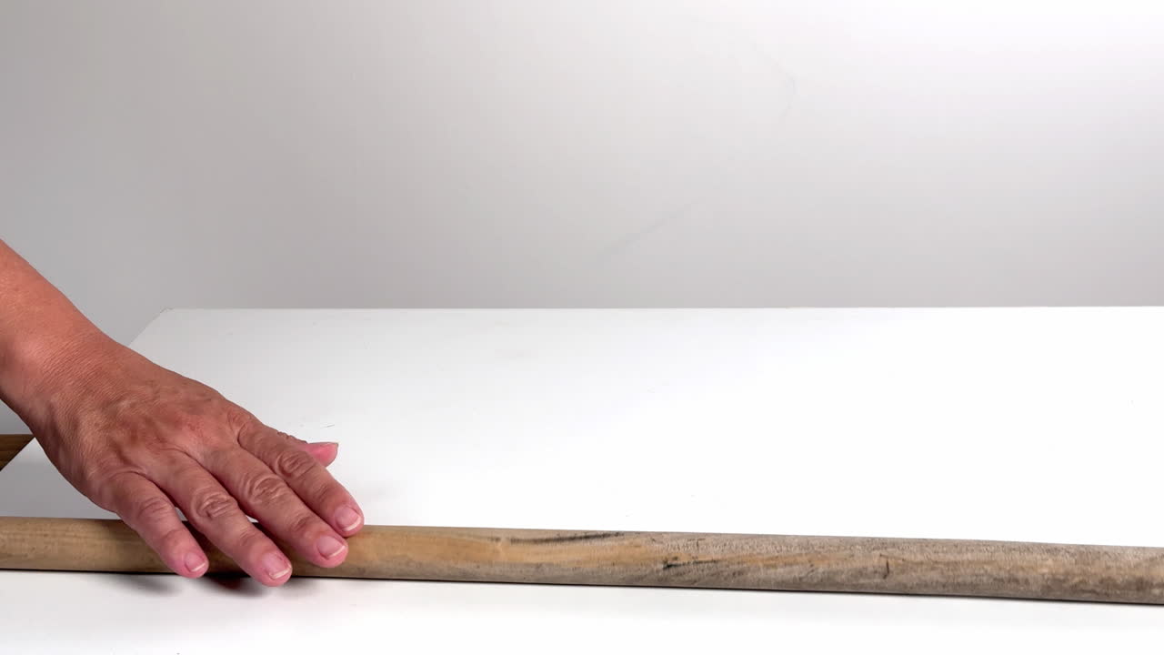 Mano che spinge un bastoncino di legno su una superficie bianca