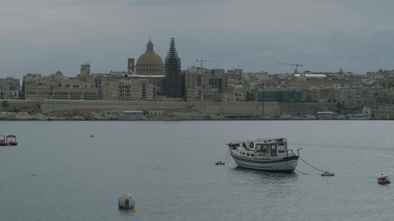 escena pacífica de un barco aislado amarrado en el puerto de valetta lanzando a lo largo de las olas con la ciudad vieja en el fondo, malta
