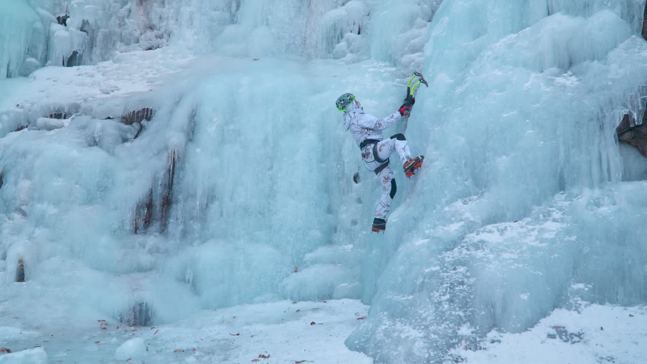 Alpinist Ice Climber Climbing a Frozen Cascade Using Two Axes on a Large Wall of Ice