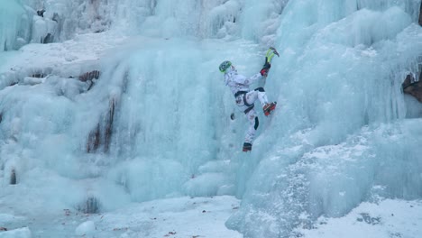 alpinist ice climber climbing a frozen cascade using two axes on a large wall of ice