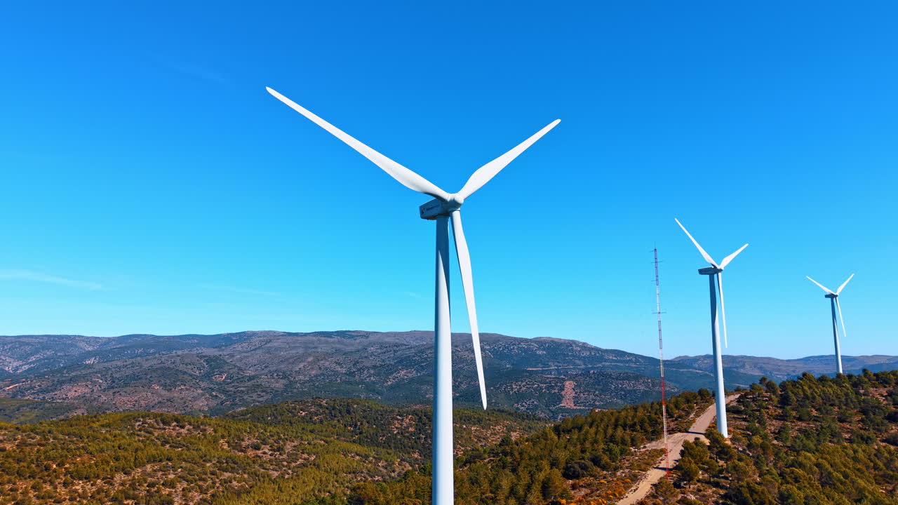 Alicante, Espanha, 8 de agosto de 2025: Turbinas eólicas ao lado de estrada de serviço em cume espanhol. Turbinas eólicas brancas, estrada no cume e mastro de comunicações em montanhas espanholas sob céu limpo.
