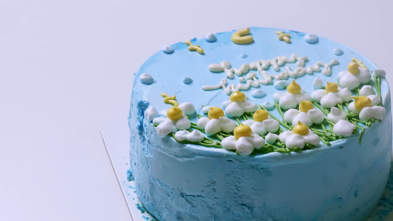 primer plano de la parte superior de un pastel de cumpleaños con glaseado azul y decorado con flores blancas y amarillas, con felicitaciones de cumpleaños en la parte superior