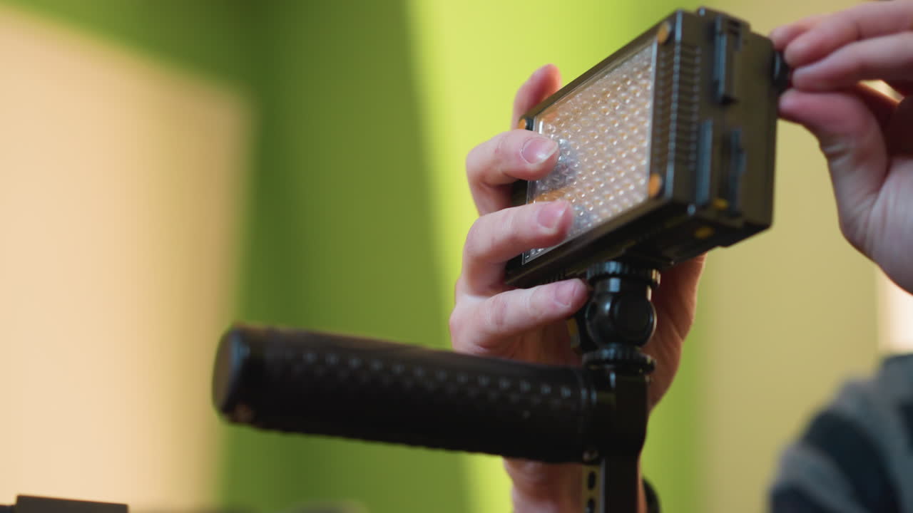 Lighting operator adjusting LED light panel while preparing camera setup for filming. Focused on adjusting lighting equipment in professional studio, ensuring proper setup for optimal lighting