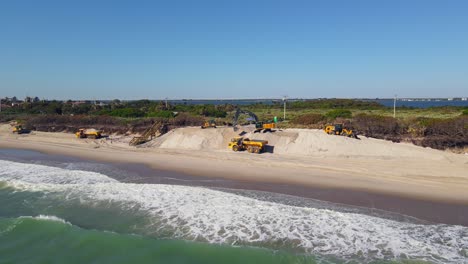 Toma-Aérea-De-Drones-De-Excavadoras-Limpiando-La-Playa-Cerca-Del-Agua-Del-Océano