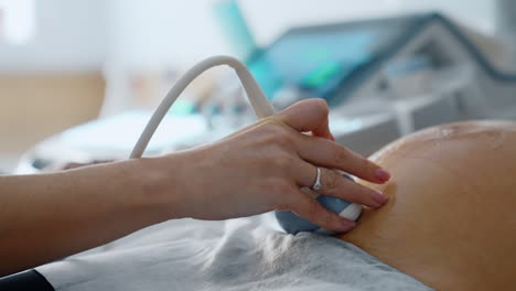 female doctor's hand moving the device of ultrasound machine by the big pregnant belly covered with gel. close up.