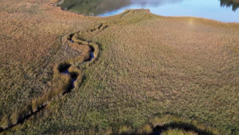 Flug-über-Einen-See-Im-Tal-Zwischen-Hügeln-Mit-Daneben-Liegender-Graslandschaft