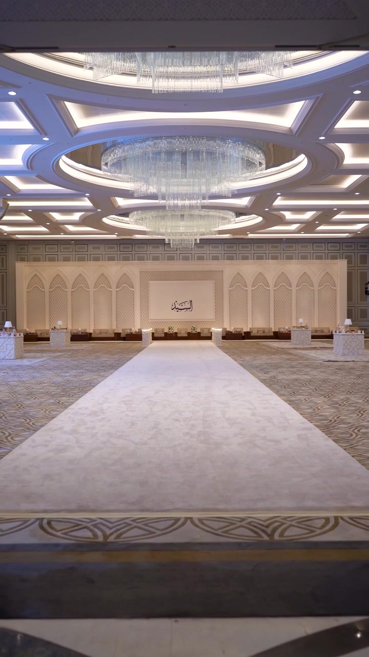 Inquadratura che attraversa un arco islamico ornato per rivelare una massiccia e vuota sala banchetti di lusso, preparata per un evento VIP a Doha