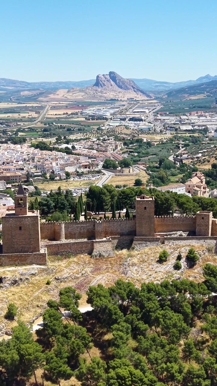 Vista aerea verticale con drone dell'Alcazaba di Antequera in Spagna con l'iconica montagna Peña de los Enamorados che si erge sopra il paesaggio circostante.