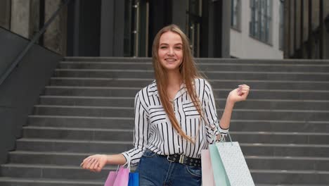 chica elegante sosteniendo bolsas de compras y mostrando los pulgares hacia arriba. regocijándose con buenos descuentos de ventas de vacaciones