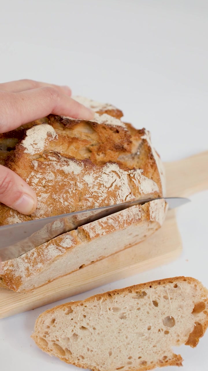 Person Slicing Fresh Crusty Sourdough Bread on Wooden Board