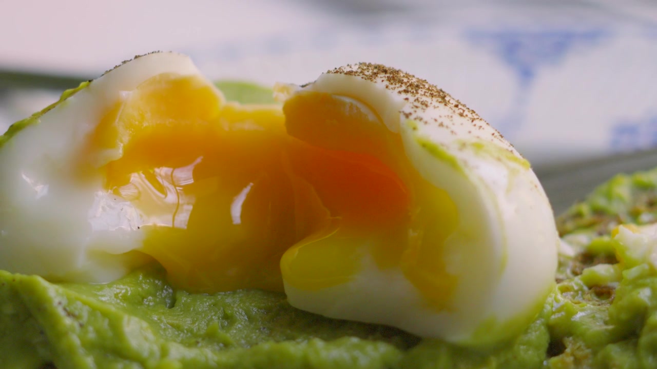 Coltello che taglia uova fresche alla coque con tuorlo dorato e avocado schiacciato su pane a lievitazione naturale. Colazione sana a basso contenuto di grassi.