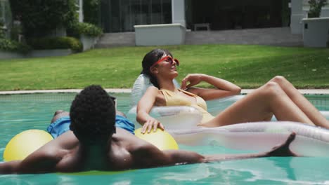 happy diverse couple wearing swimming suits with inflatables at swimming pool in garden