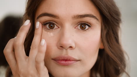 focused lady blends liquid concealer under eyes with finger