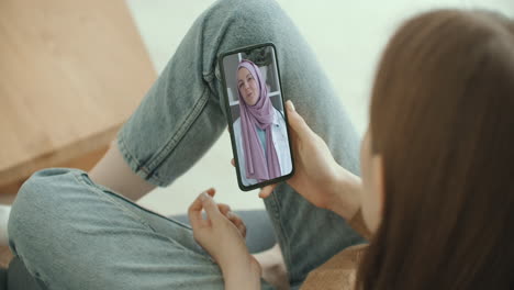 Frau-Nutzt-Medizinische-App-Auf-Dem-Smartphone-Und-Berät-Sich-Per-Videokonferenz-Mit-Einer-Arabischen-Muslimischen-Frau-Im-Hijab-Arzt.-Frau-Nutzt-Online-Chat,-Um-Mit-Familientherapeuten-Und-Einer-Coronavirus-Pandemie-Zu-Sprechen.