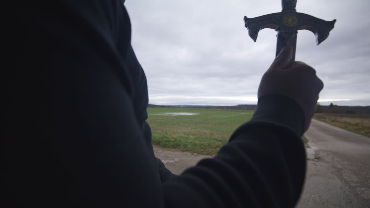 현대의 검은 검사 전사는 회색 하늘 아래 야외에서 대결 상대를 기다리고 있습니다. - 유럽, 4k - 근육, 협박, 그림자, 형상, 흐릿한, 어두운 옷, 강력한, 가까운, 손, 듀얼