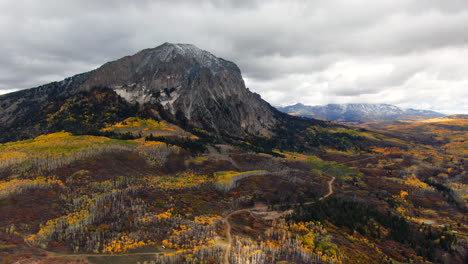 dramatic road sunny cloudy autumn aspen tree fall colors kebler pass aerial cinematic drone snow on peaks landscape crested butte gunnison colorado early fall red yellow orange rocky mountains forward