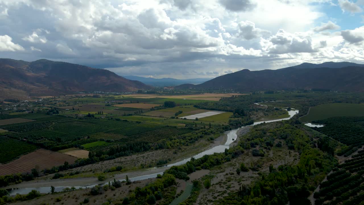 órbita aérea de campos de cultivo verdes y río corriente, montañas en el fondo en un día nublado, valle de cachapoal, al sur de santiago, chile
