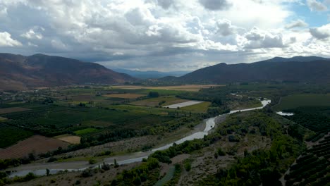 órbita aérea de campos de cultivo verdes y río corriente, montañas en el fondo en un día nublado, valle de cachapoal, al sur de santiago, chile