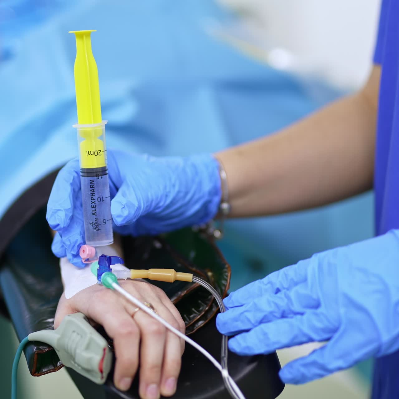 Gloved hands of a doctor make injection to a patient. Tubes connected to the patient's hand at operation. Close up