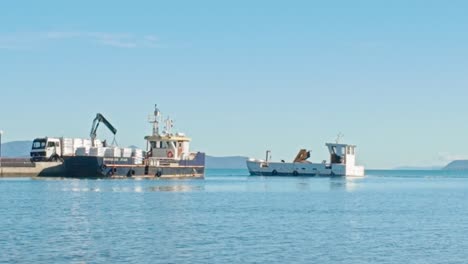 loading cargo by crane onto coastal sea barge from dockside lorry