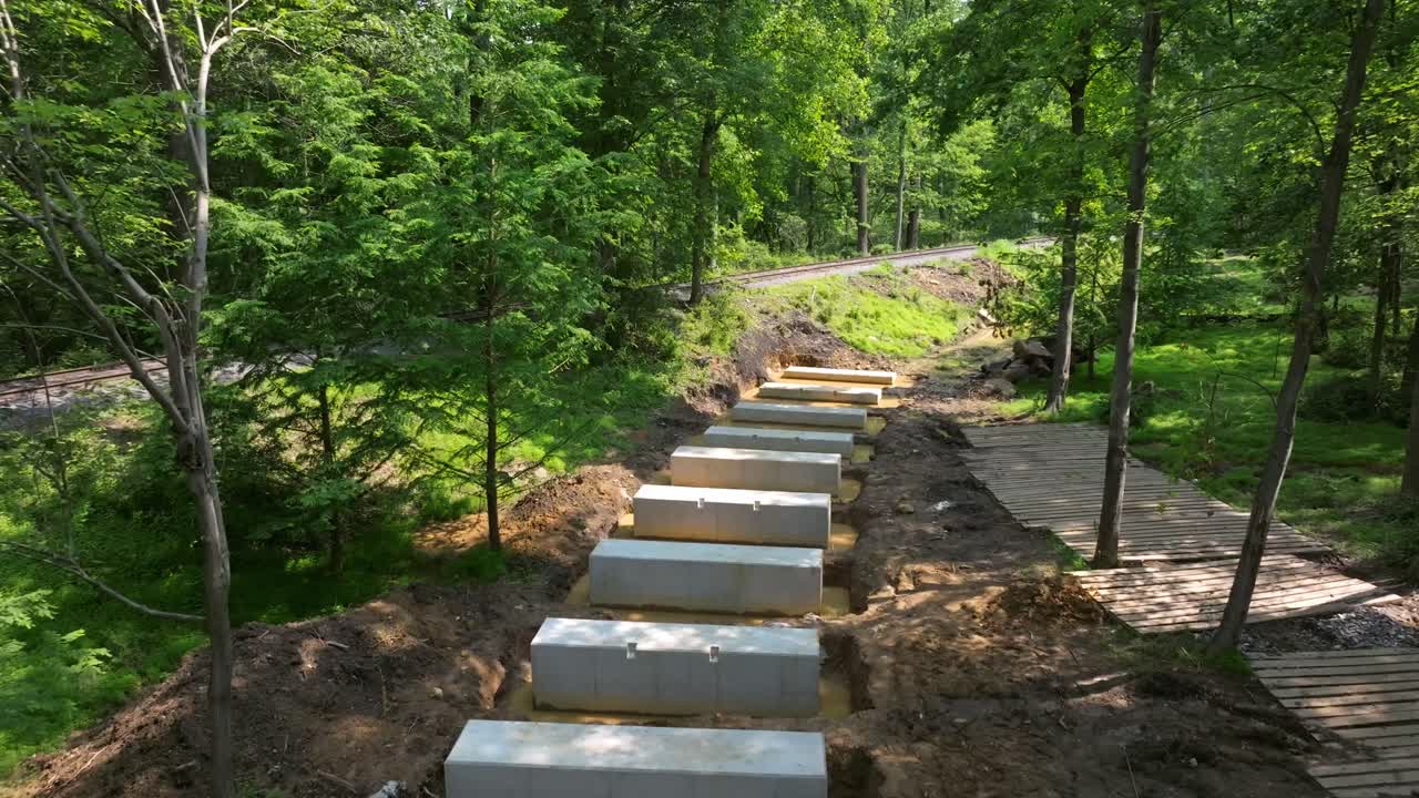 Workers are installing concrete blocks to create a New Rail Road Trestle through a lush forest. The project aims to enhance accessibility amidst the natural landscape