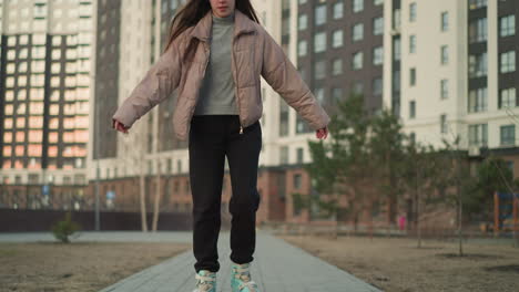 a young woman wearing a peach jacket and black trousers is rollerblading with a smile through a modern urban area. the background features tall residential buildings and trees